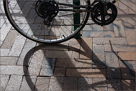 Bicycle photography - Wheel casting shadow on Toole Avenue sidewalk, Downtown Tucson, Arizona